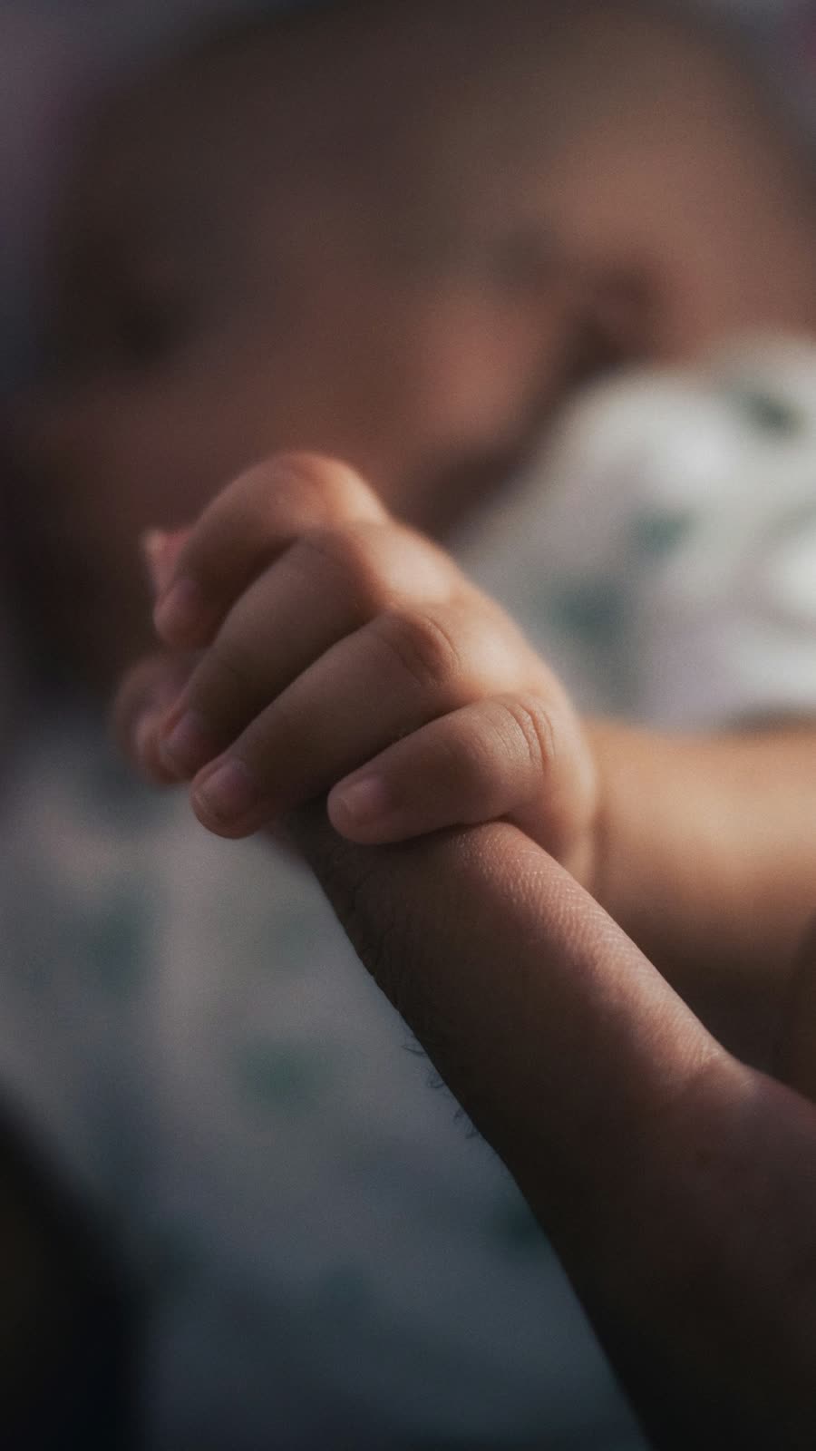 A baby's tiny hand gripping an adult's finger